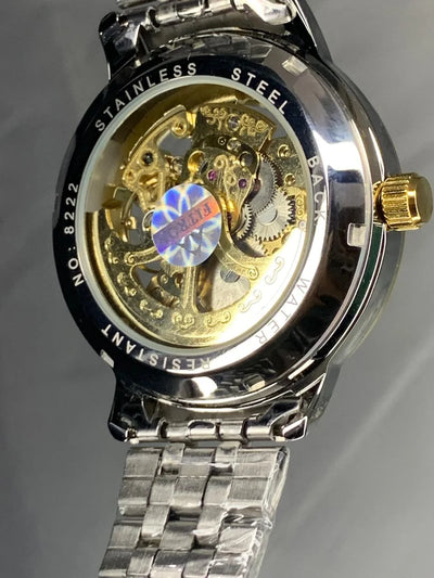 Mechanical watch with visible gears and 'Stainless Steel' text on a gray background