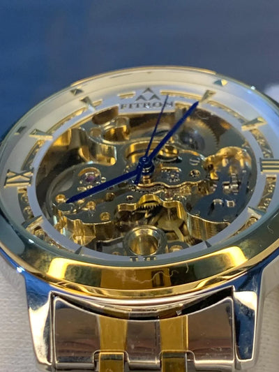 Gold and silver watch with visible mechanical components on a blue background