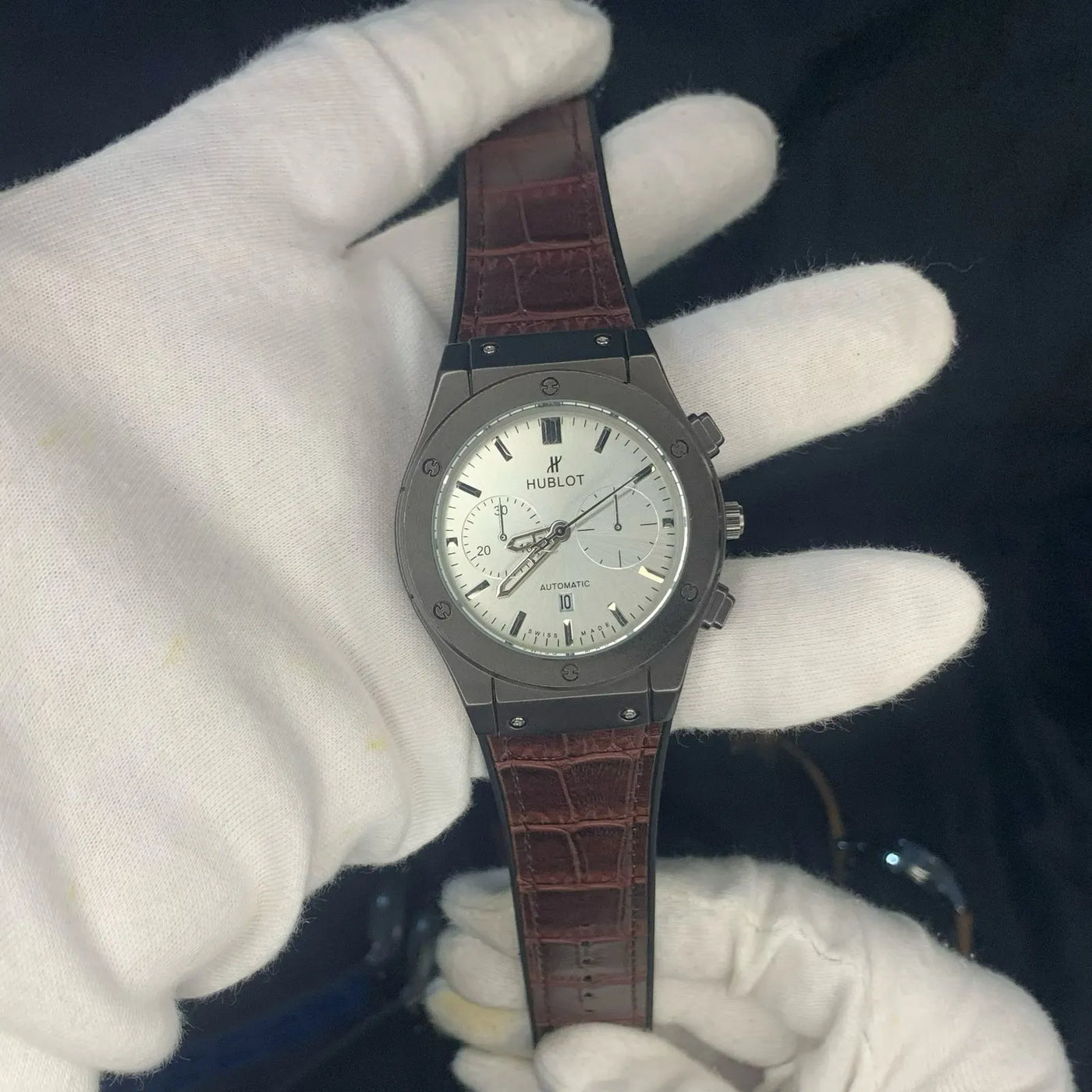 Hublot watch held by a gloved hand against a dark background