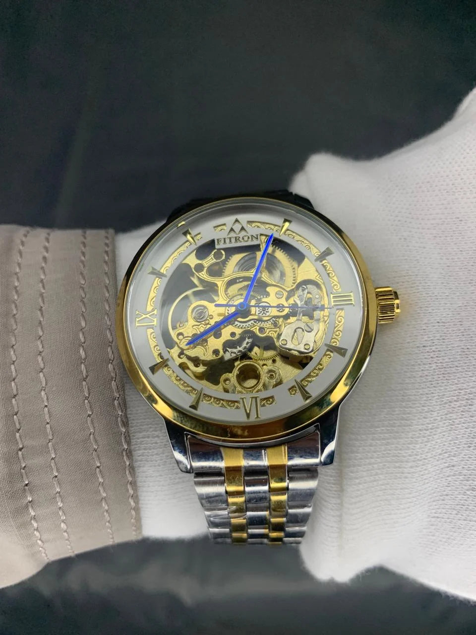 Gold and silver watch with intricate design on a white cloth