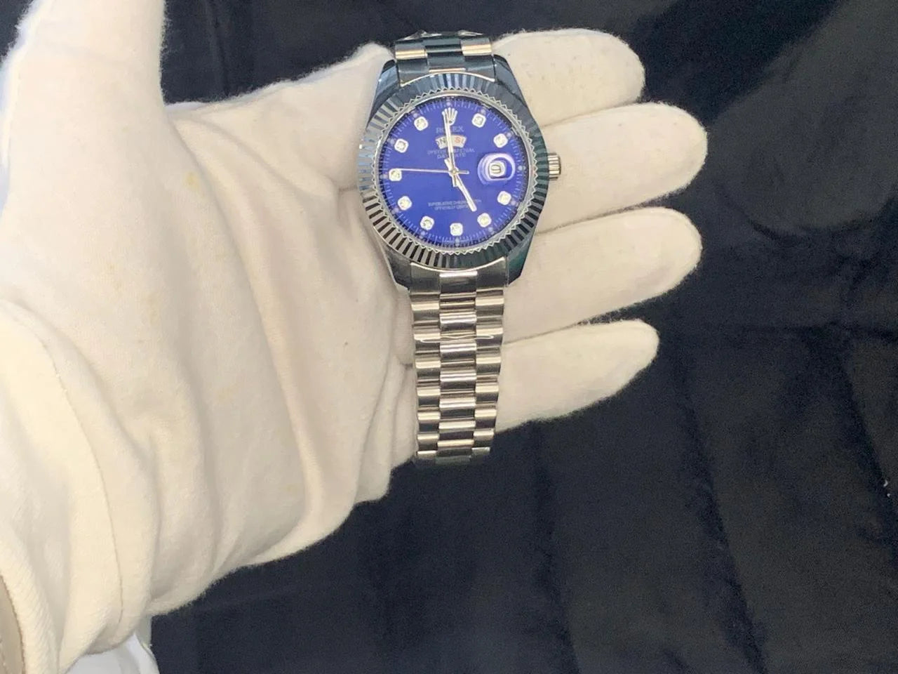 Watch with a blue face held by a gloved hand against a dark background