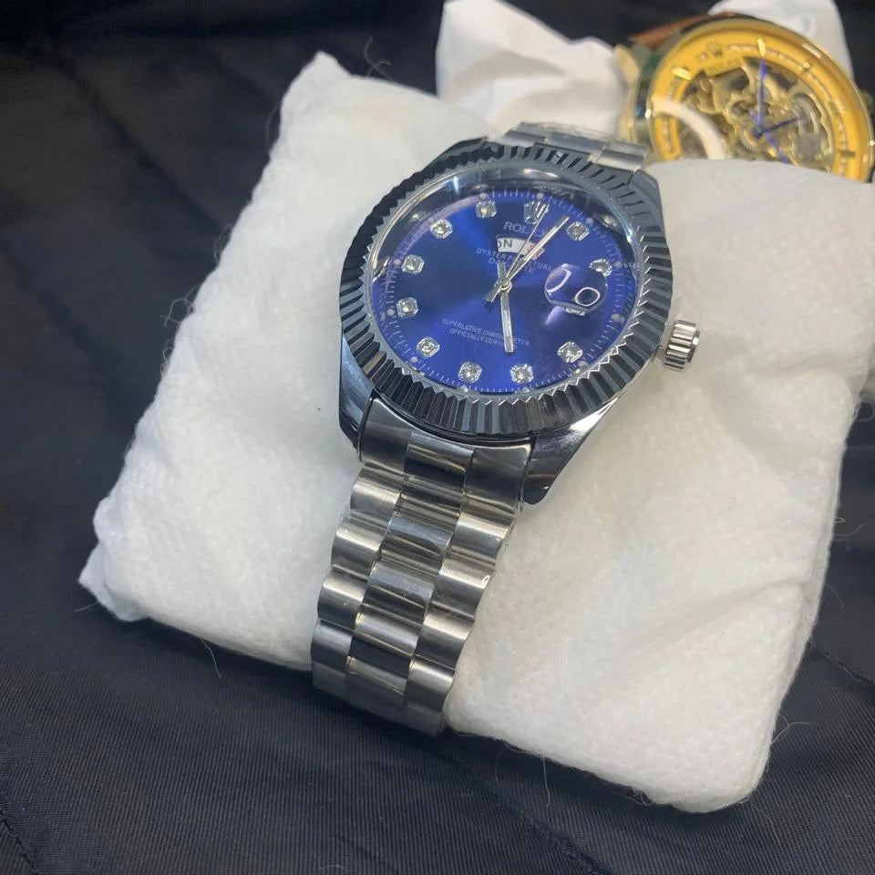 Watch with blue face and silver case on a white cushion against a dark background