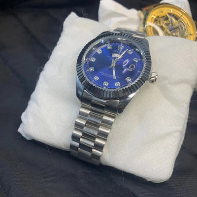 Watch with blue face and silver case on a white cushion against a dark background