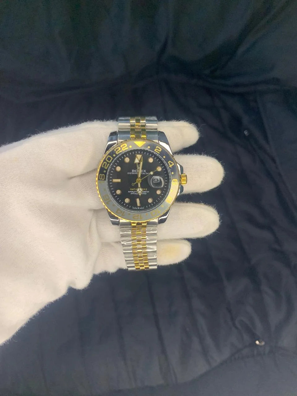 Luxury watch with gold and silver band on a white glove against a dark background