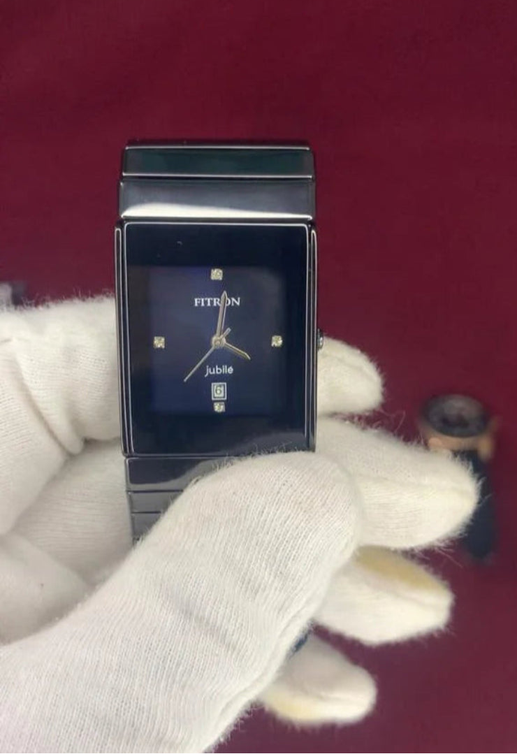Black rectangular watch on a red surface with a white glove