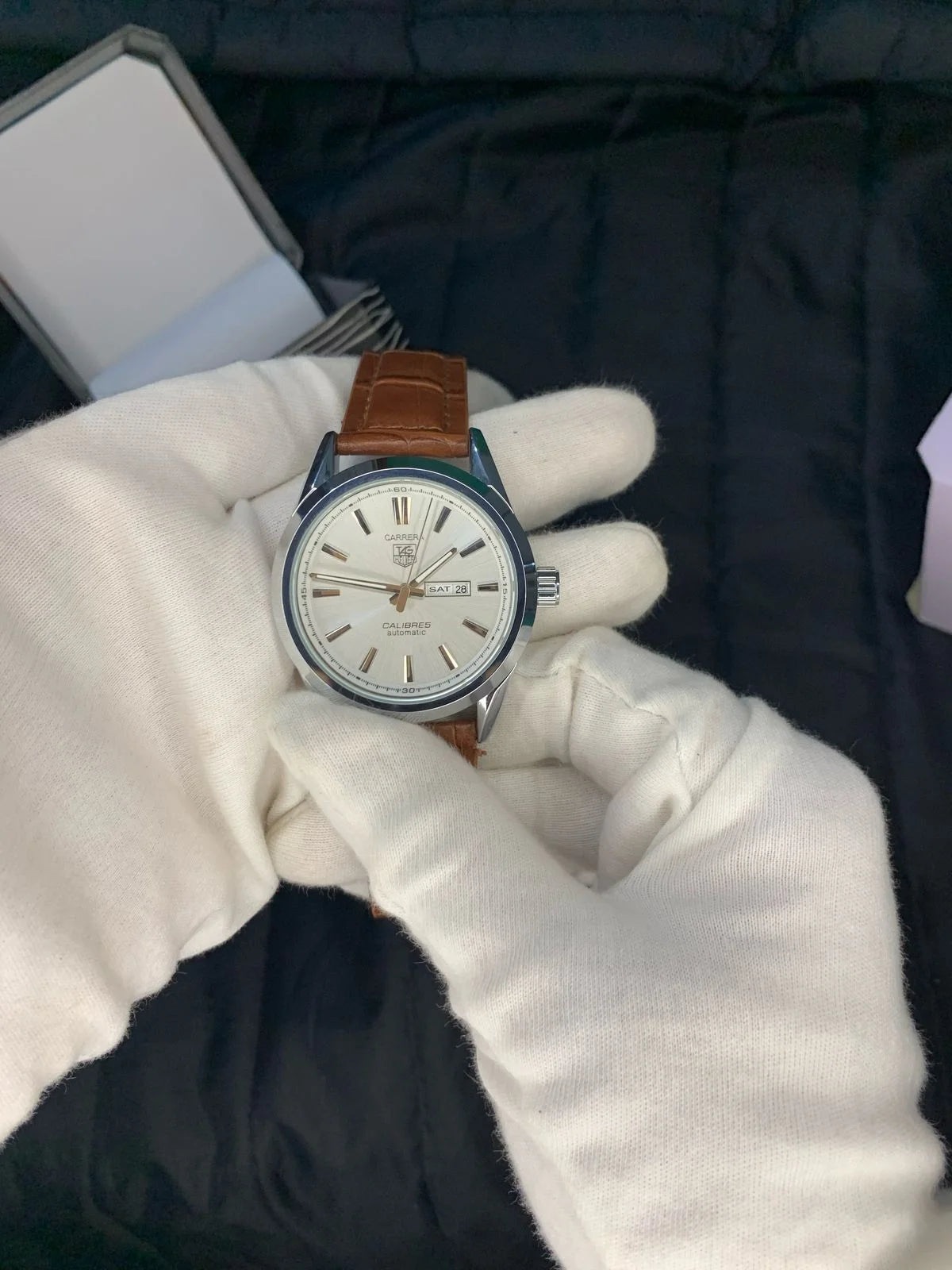 Watch held by a gloved hand with a dark background