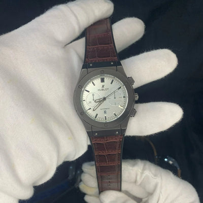 Watch with brown leather strap held by a gloved hand against a dark background