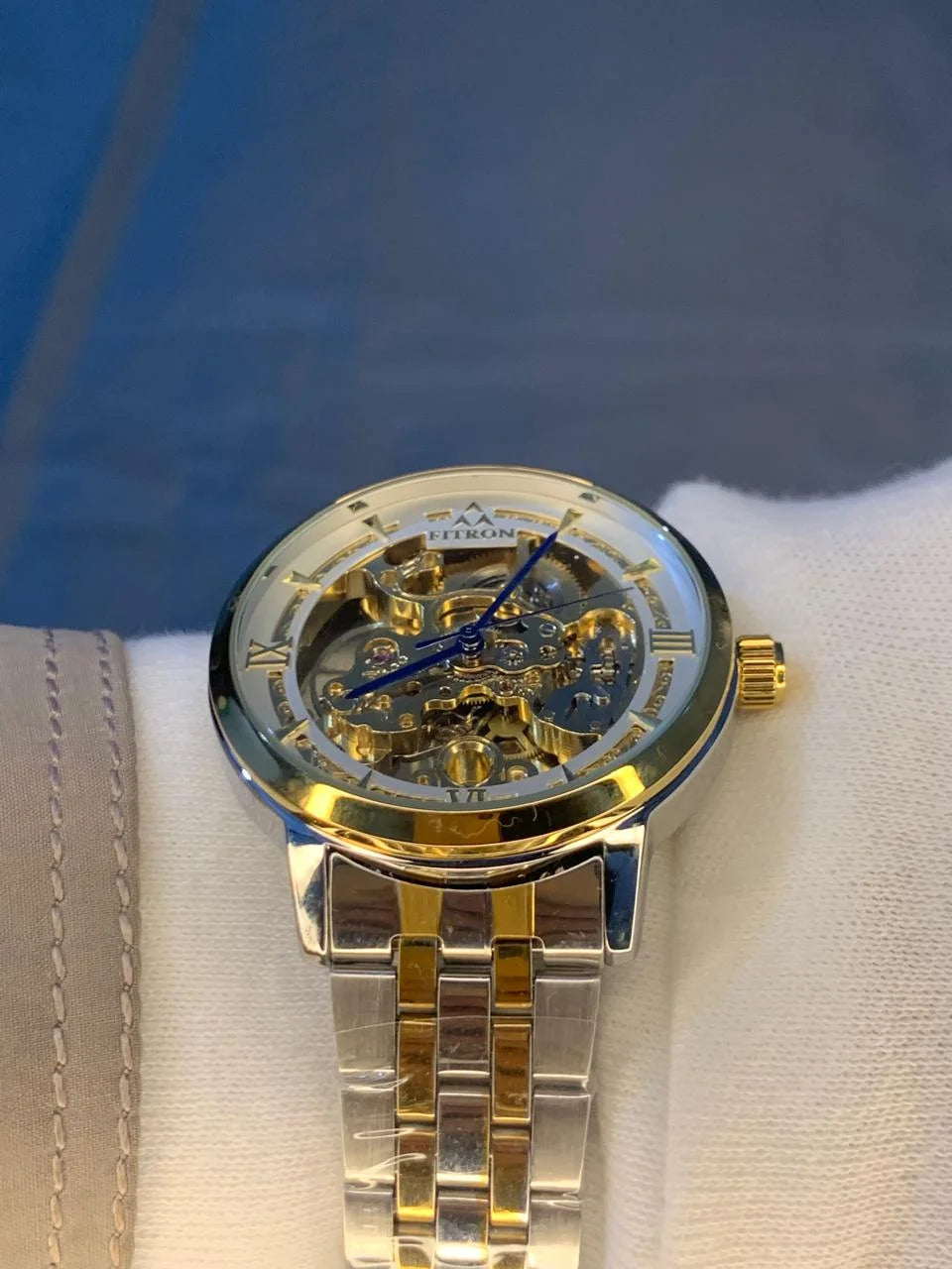 Gold and silver watch on a white cushion with a blue background