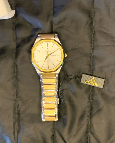 Gold watch on a black textured surface with a visible brand tag.
